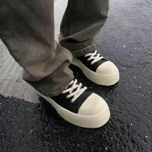 Black low-top platform sneakers worn with loose gray denim on wet urban pavement in a casual streetwear outfit