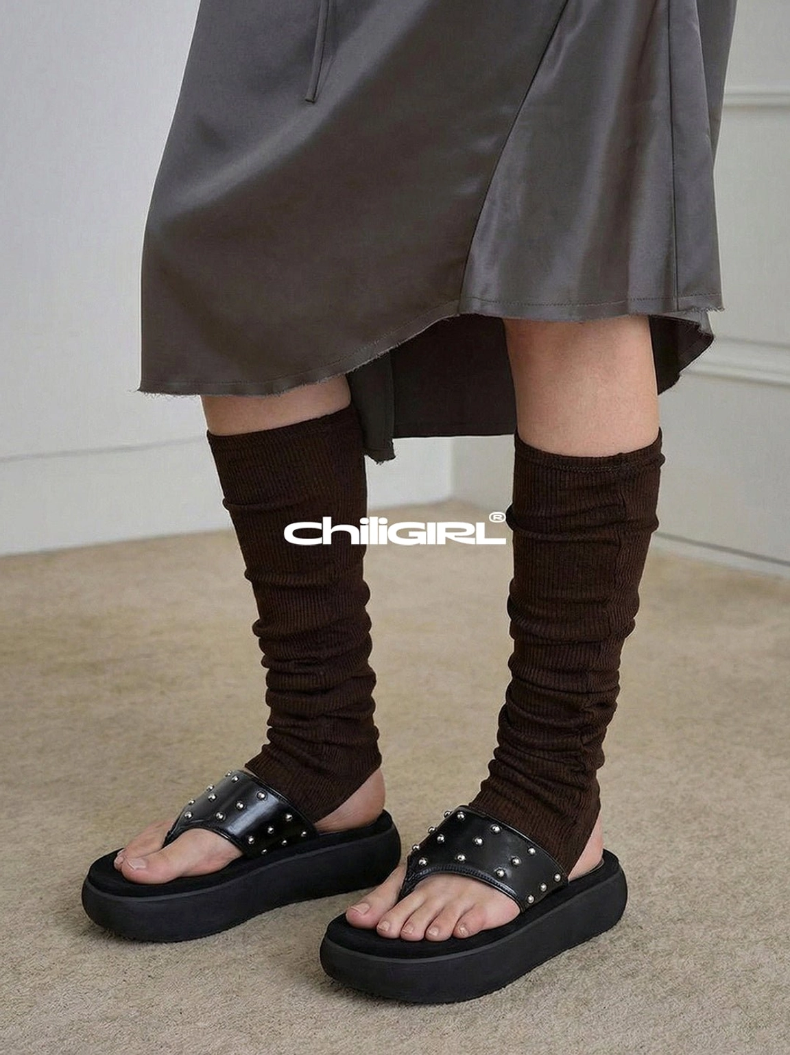 Black studded platform thong sandals styled with brown leg warmers and a gray midi skirt