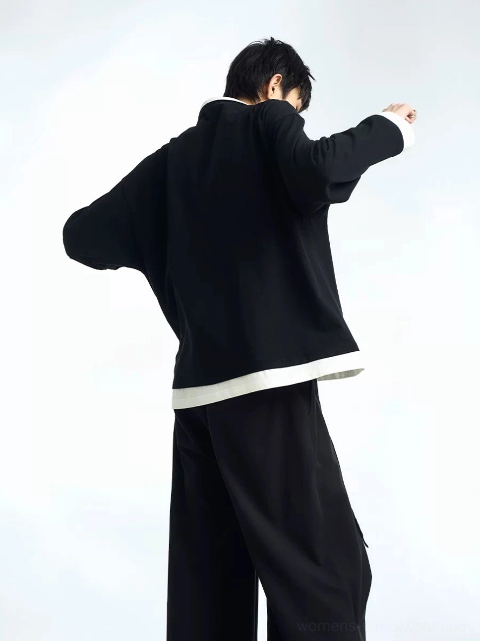 Back view of black pleated balloon wide-leg streetwear pants worn with an oversized black sweater, showing the relaxed draped silhouette and full rear fit