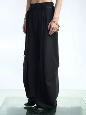 Black pleated balloon wide-leg streetwear pants shown in a front three-quarter view with oversized loose legs, high waist, smooth suiting fabric, and layered silver streetwear jewelry