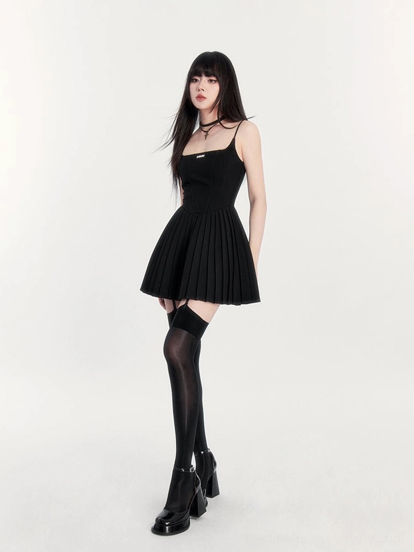 Black pleated cami mini dress shown from the side with square neckline fitted bodice stocking and chunky heeled shoes