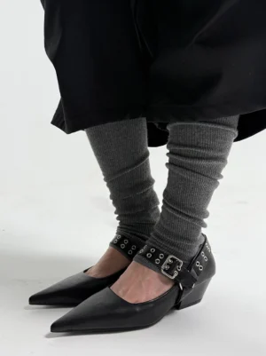 Black pointed buckle-strap Mary Jane pumps worn with charcoal ribbed leg warmers and a long black streetwear coat