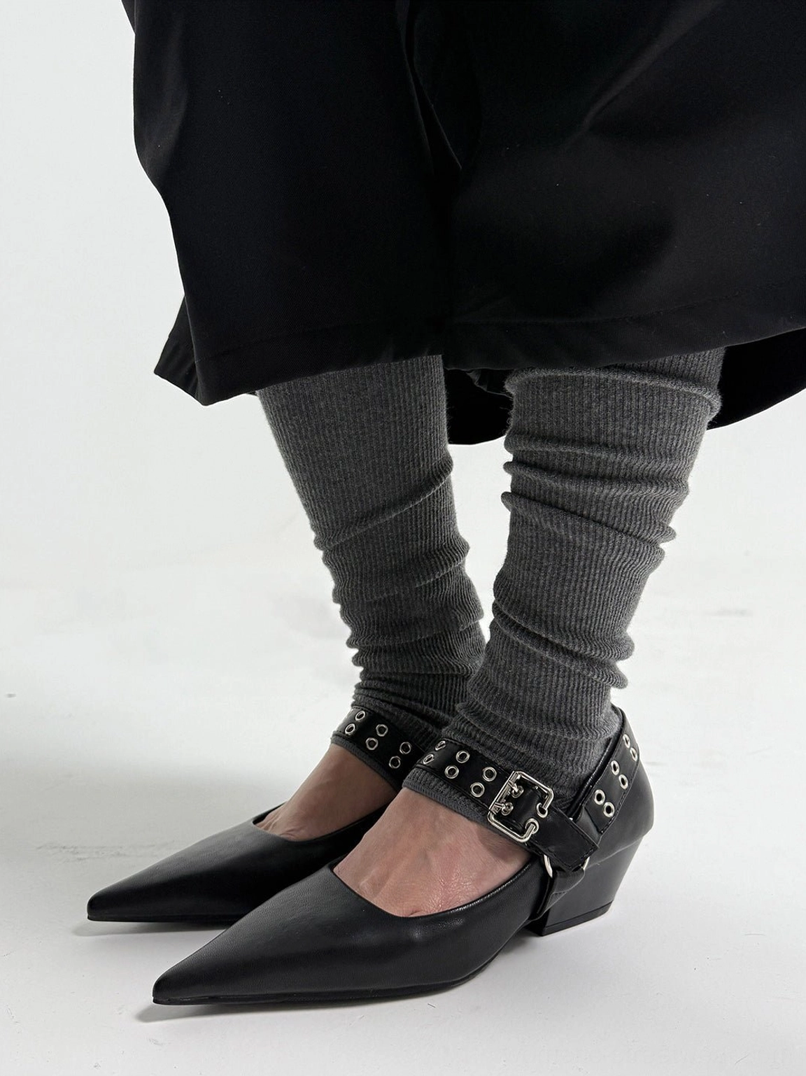 Black pointed buckle-strap Mary Jane pumps worn with charcoal ribbed leg warmers and a long black streetwear coat