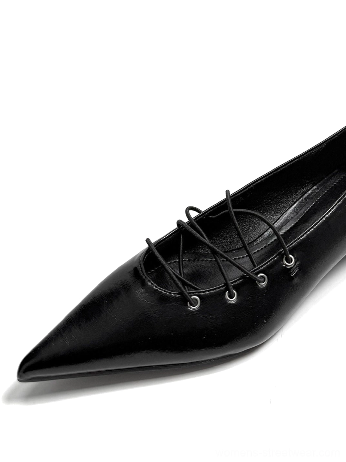 Close-up of a black pointed lace-up ballet flat showing detailed crisscross laces, metal eyelets, sharp toe, and glossy finish