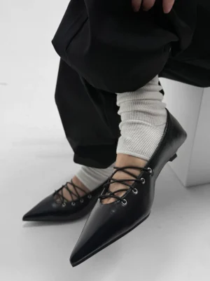 Worn black pointed lace-up ballet flat styled with white slouch socks and loose black trousers in a Korean streetwear outfit