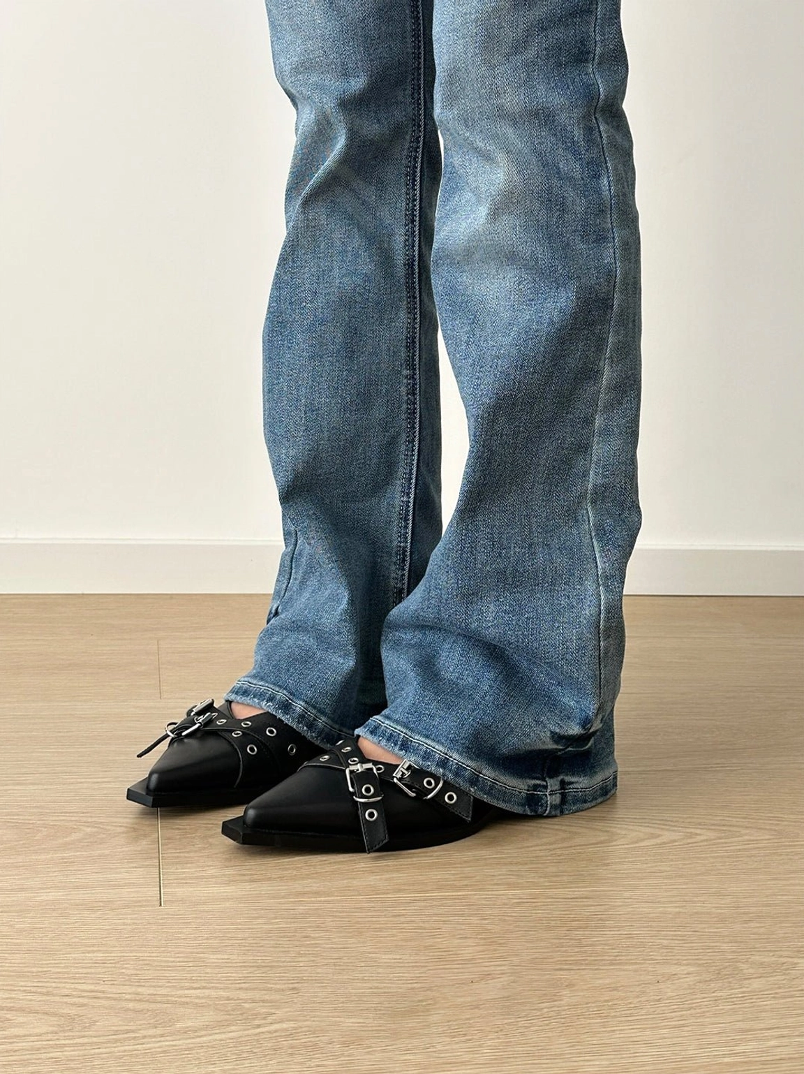 Front view of black pointed Mary Jane flats with layered silver buckle straps worn with blue flared denim jeans