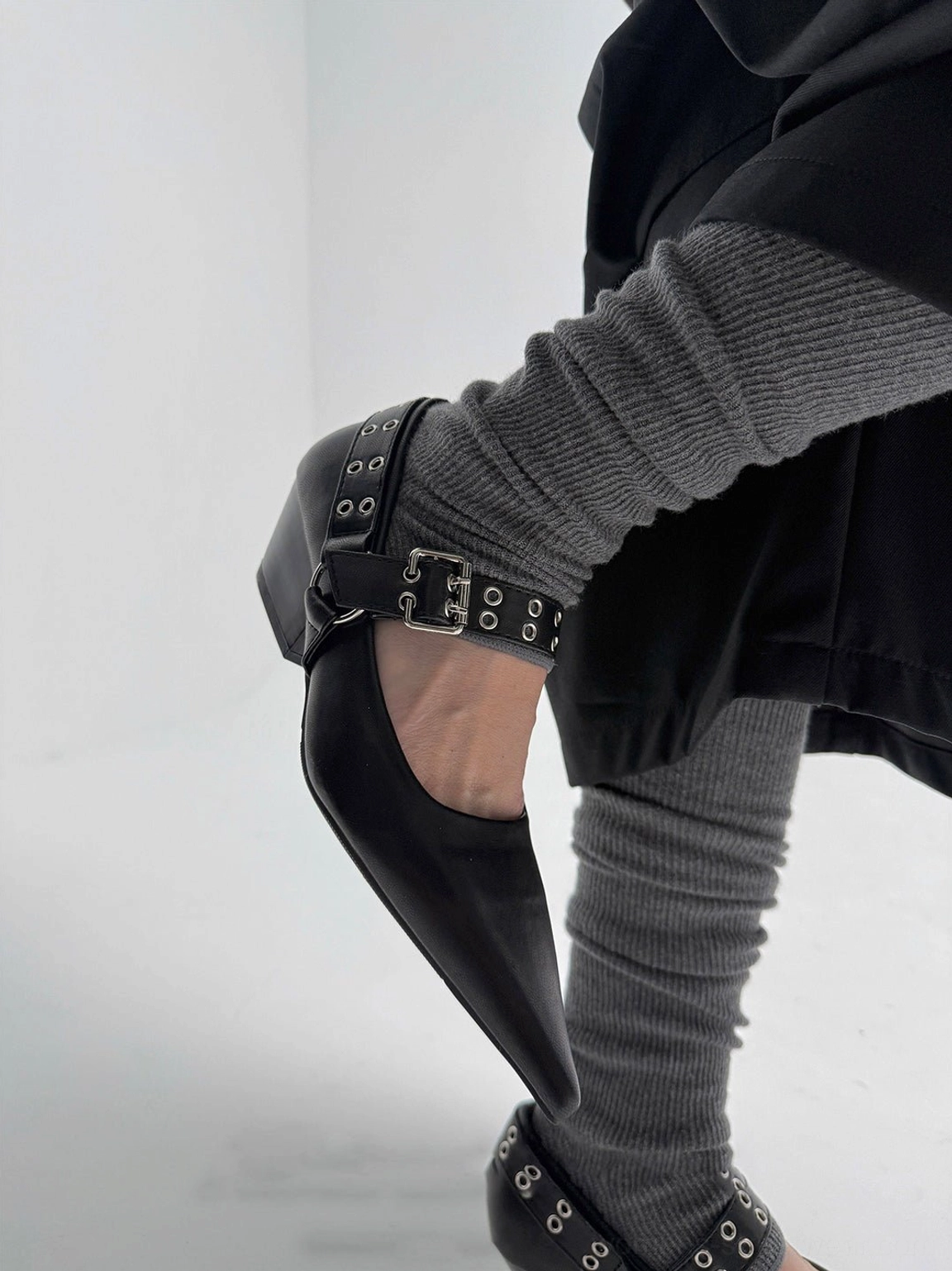 Black pointed Mary Jane pump worn in a three-quarter view showing the adjustable metal buckle and eyelet ankle strap