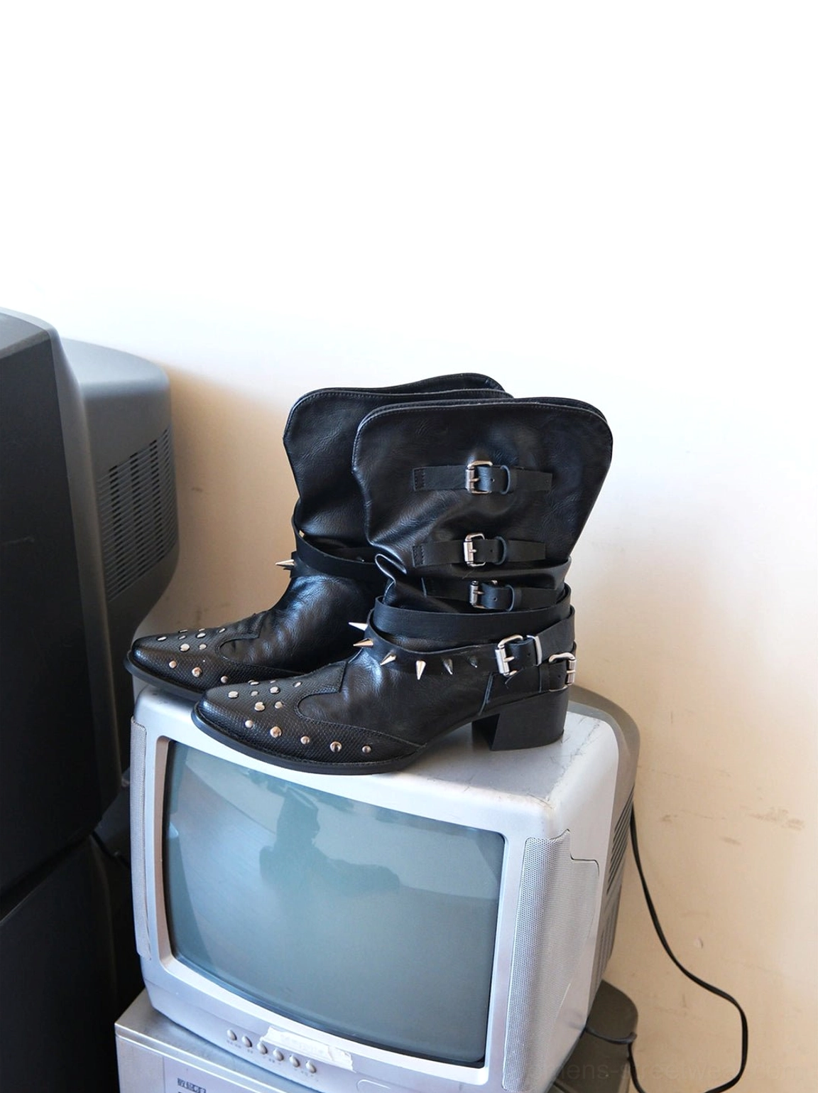 Black pointed-toe ankle boots with silver buckles and studded toe displayed beside a vintage television