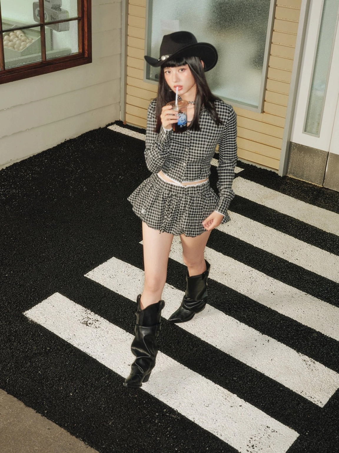 Female model wearing black pointed-toe knee-high cowboy boots with a houndstooth outfit and cowboy hat at night