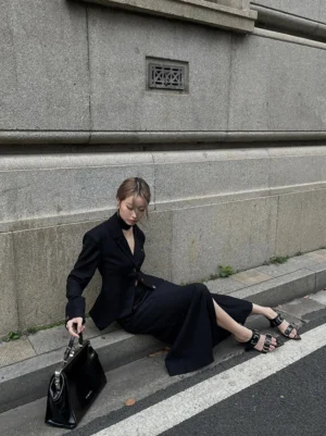 Model wearing black pointed-toe wedge sandals with a tailored all-black suit in an urban streetwear setting