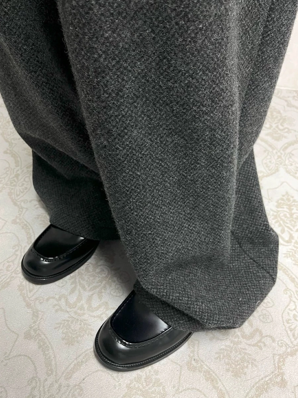 Black polished leather loafers styled with grey wool trousers in a coordinated formal streetwear outfit