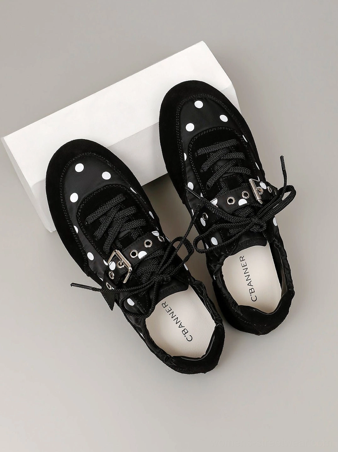 Top-down flat lay of black polka dot ballet sneakers showing lace-up closure, instep buckle strap, and suede-look trim