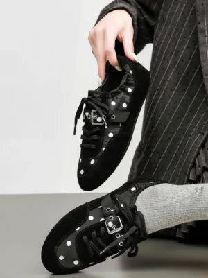 Close-up lifestyle view of black polka dot ballet sneakers with silver buckle strap styled with striped coat and gray socks