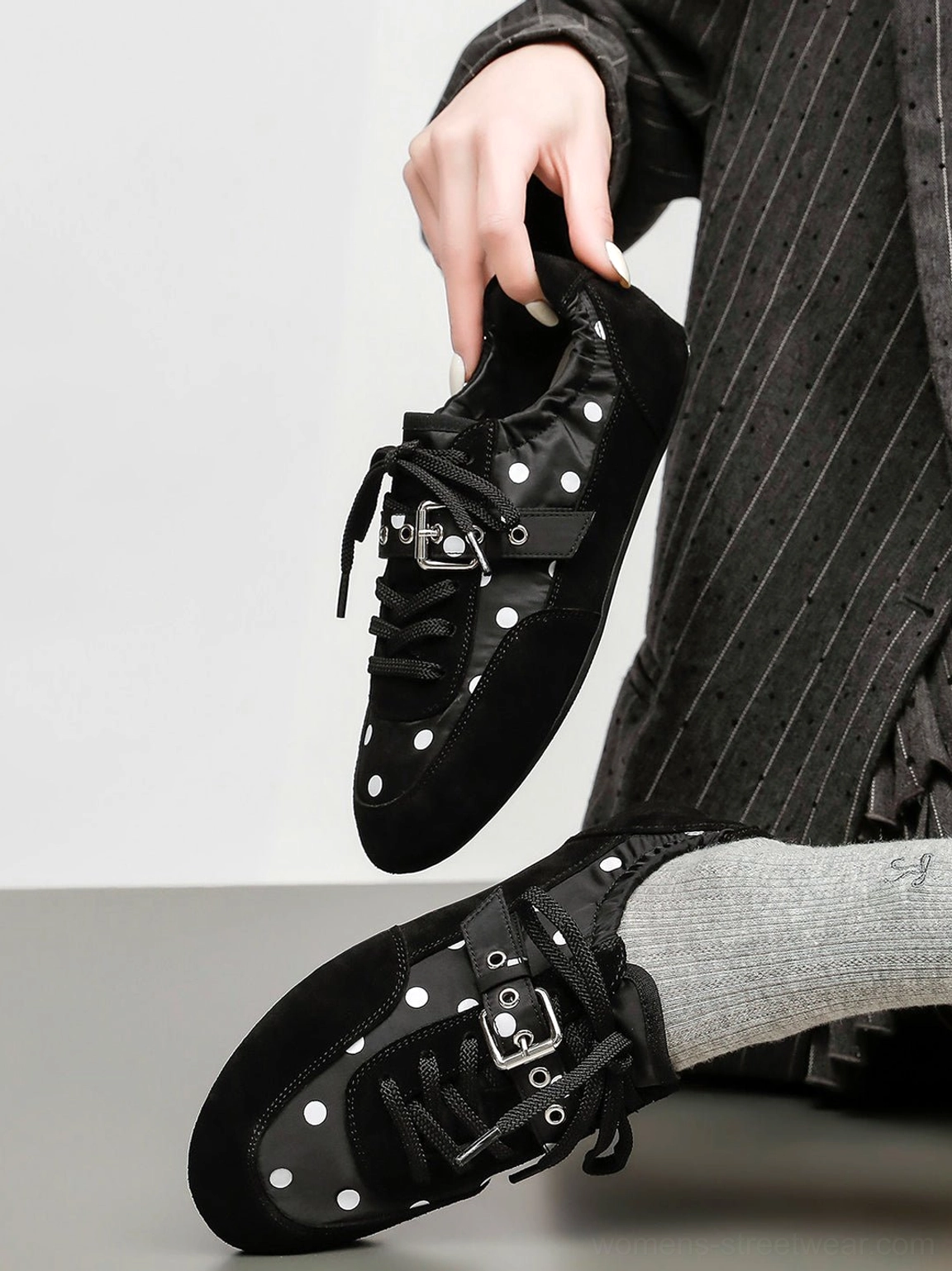 Close-up lifestyle view of black polka dot ballet sneakers with silver buckle strap styled with striped coat and gray socks