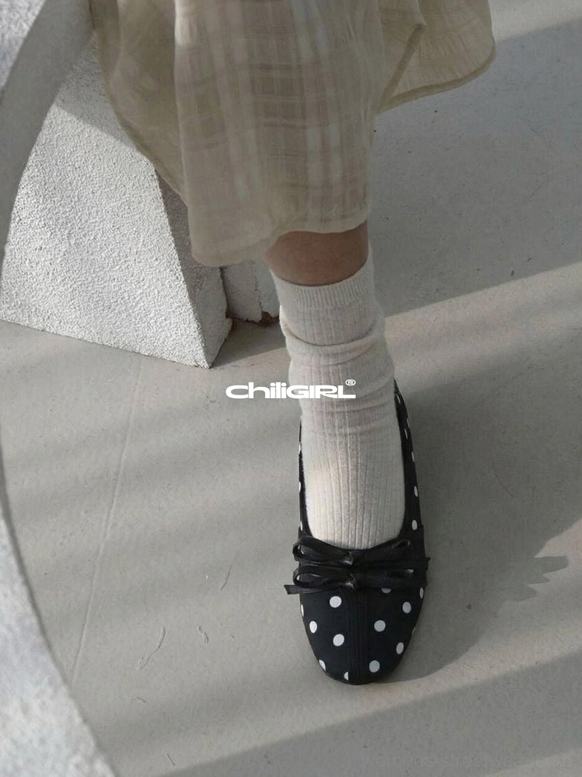 Black polka dot bow ballet flats worn with short white socks and a light grey midi skirt