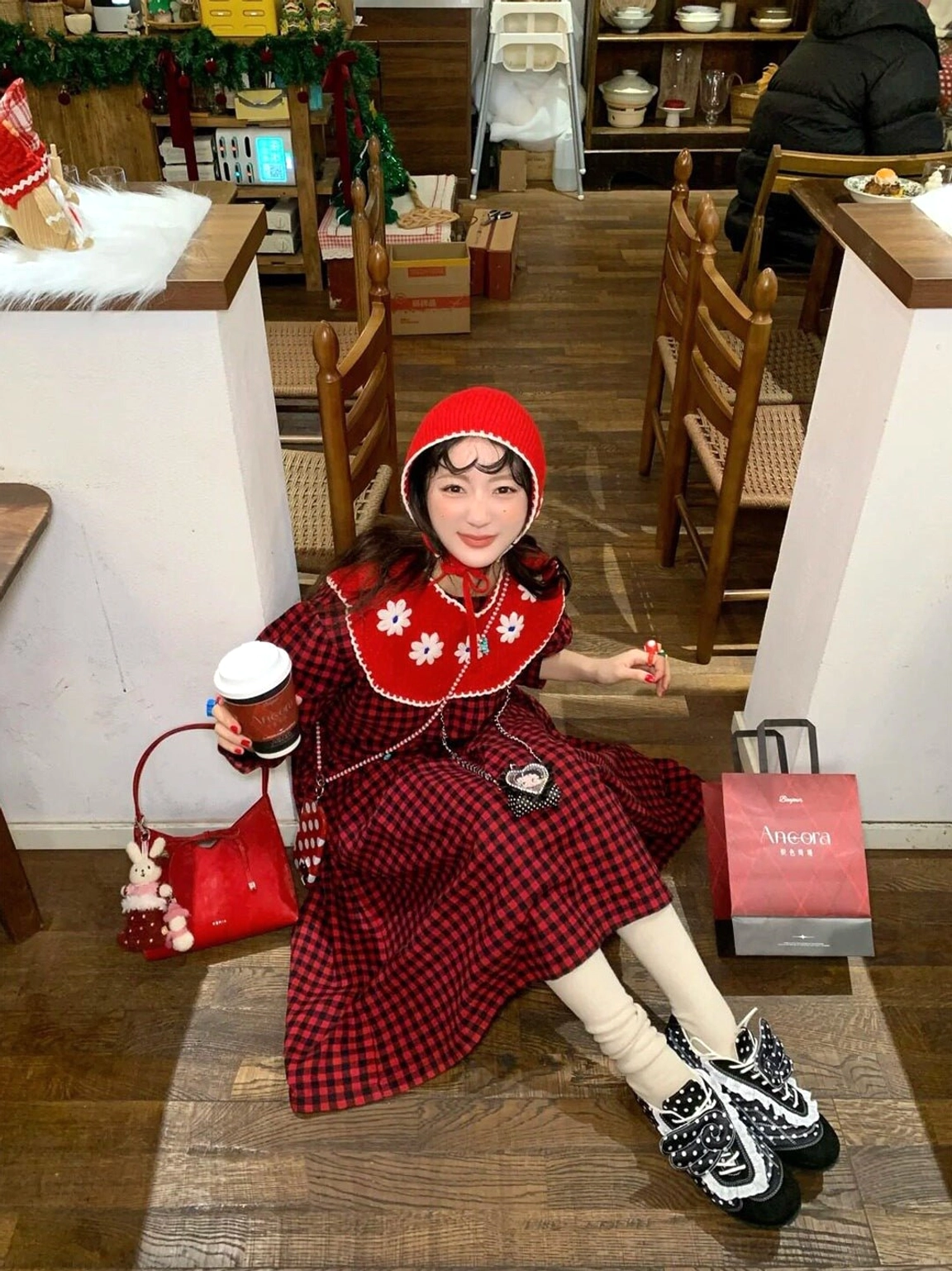 Black polka dot lace ballet flats worn with white socks and a red plaid dress in a cozy cafe setting