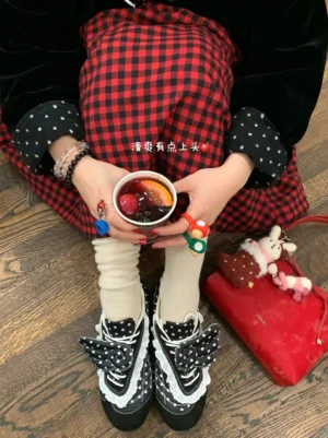 Top view of black polka dot lace wing ballet flats styled with white socks, a red plaid skirt, red handbag, and coffee drink