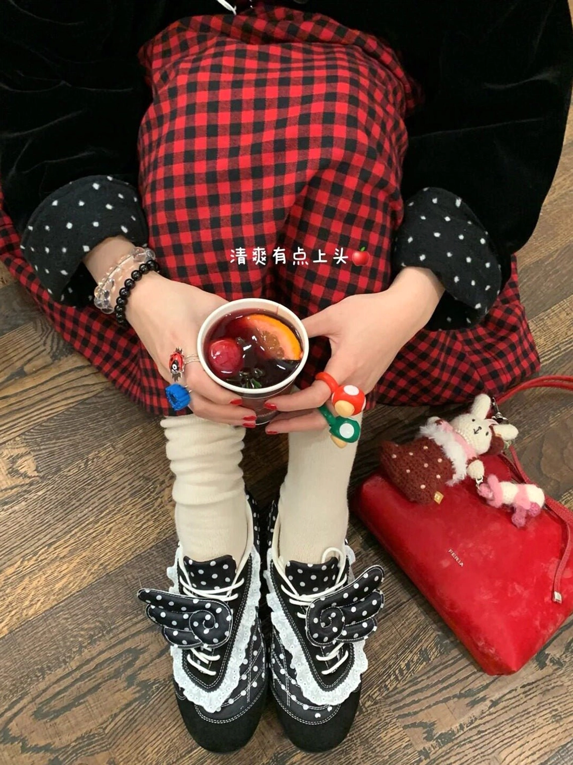 Top view of black polka dot lace wing ballet flats styled with white socks, a red plaid skirt, red handbag, and coffee drink