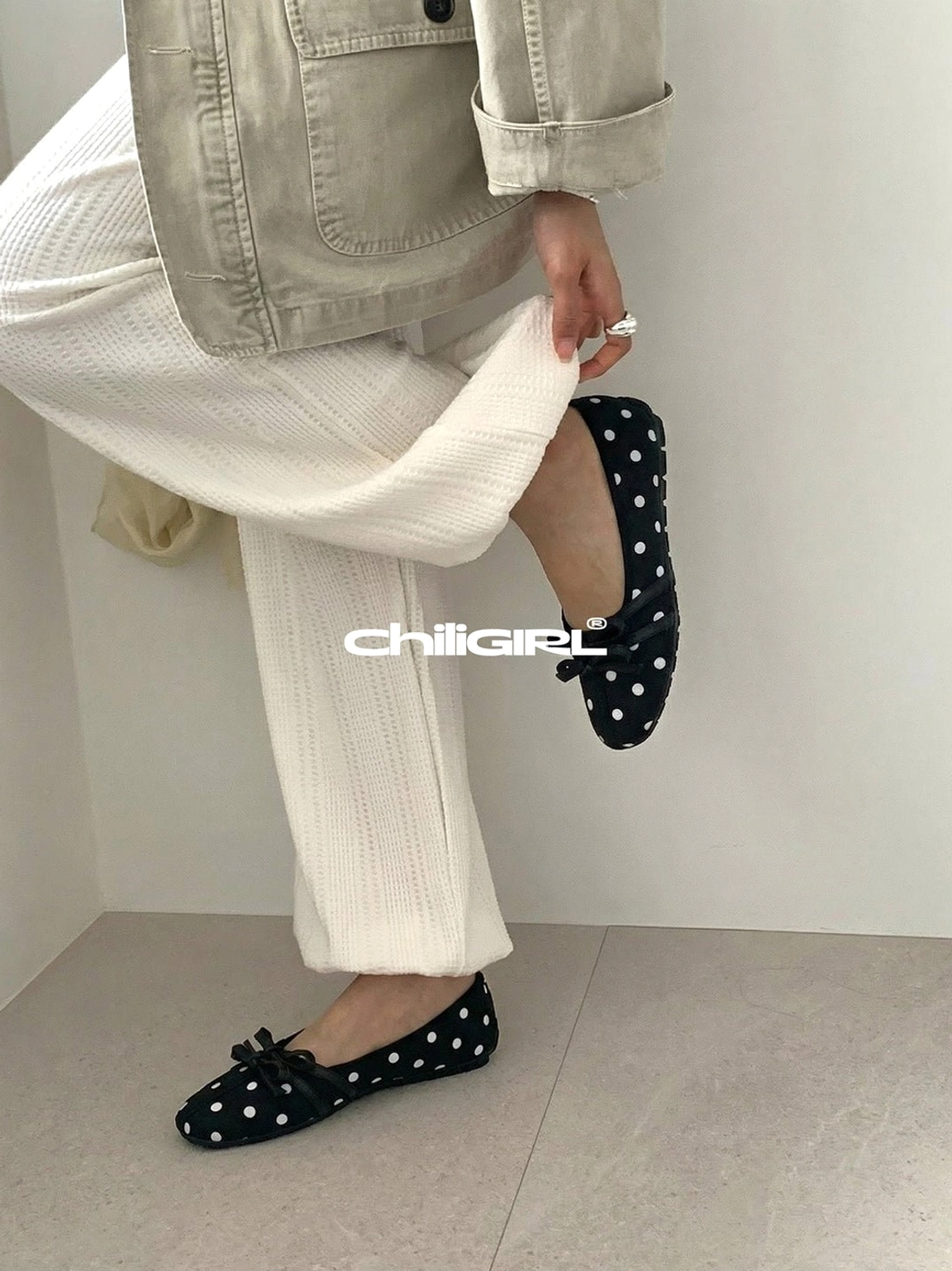 Side view of black polka dot Mary Jane ballet flats worn with off-white ribbed trousers for a minimalist outfit