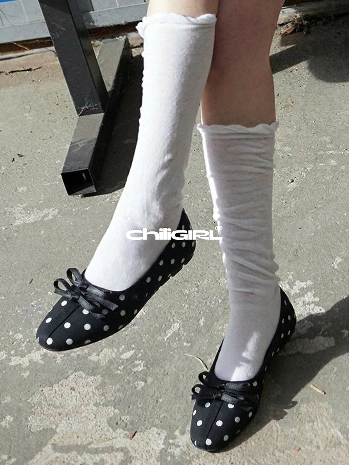 Black polka dot Mary Jane flats with front bows worn with long white ruffled socks in an outdoor streetwear setting