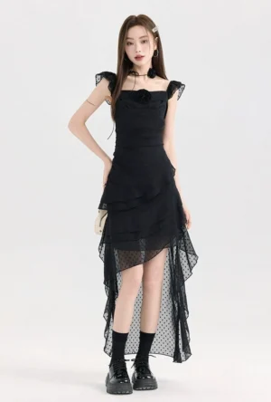 Black polka dot mesh ruffle high-low dress shown in a full-body three-quarter view with square neckline, floral chest detail, asymmetrical sheer tulle hem, and platform boots