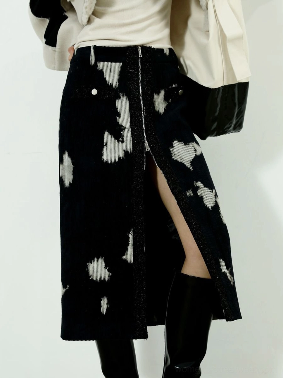 Close-up view of black printed corduroy midi skirt with central front zipper slit and decorative pocket buttons