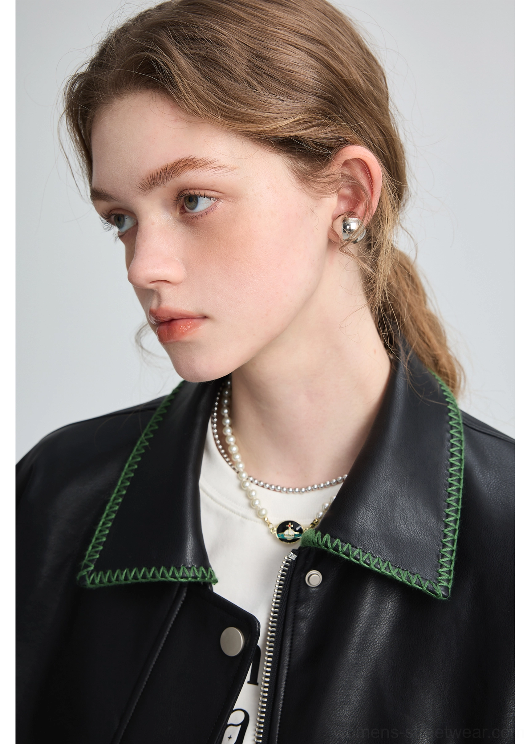 Close-up of black PU leather biker jacket collar with green contrast stitching, snap closure, and layered pearl necklaces