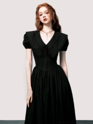 Close-up of black puff sleeve midi dress showing fold-over V-neck collar, front bow detail, layered necklace styling, and fitted waist
