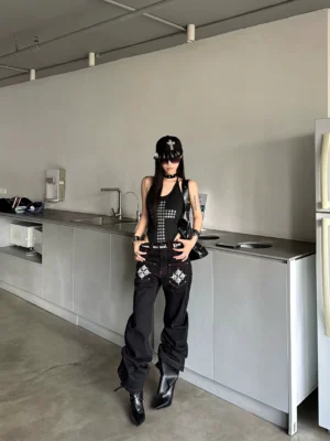 Front view of black punk graphic wide-leg jeans with red contrast stitching and white cross embroidery styled with heeled boots