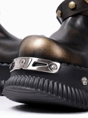 Close-up of black punk platform ankle boot toe with distressed brown-black finish, polished metal toe hardware, studded strap, and ridged rubber sole
