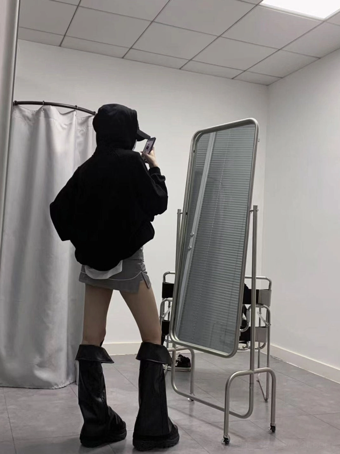 Black punk platform knee-high boots styled with a black hoodie and mini skirt in a fitting room mirror outfit view