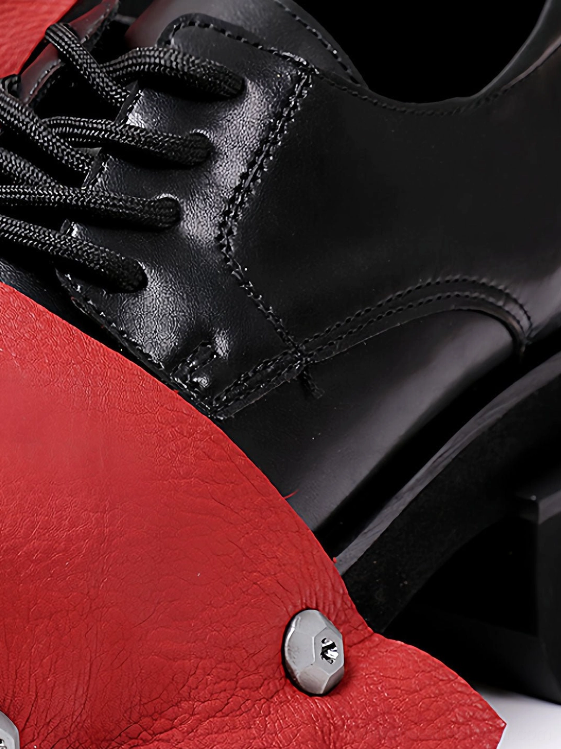 Close-up of polished black lace-up upper with pebbled red rivet overlay on square-toe derby shoe