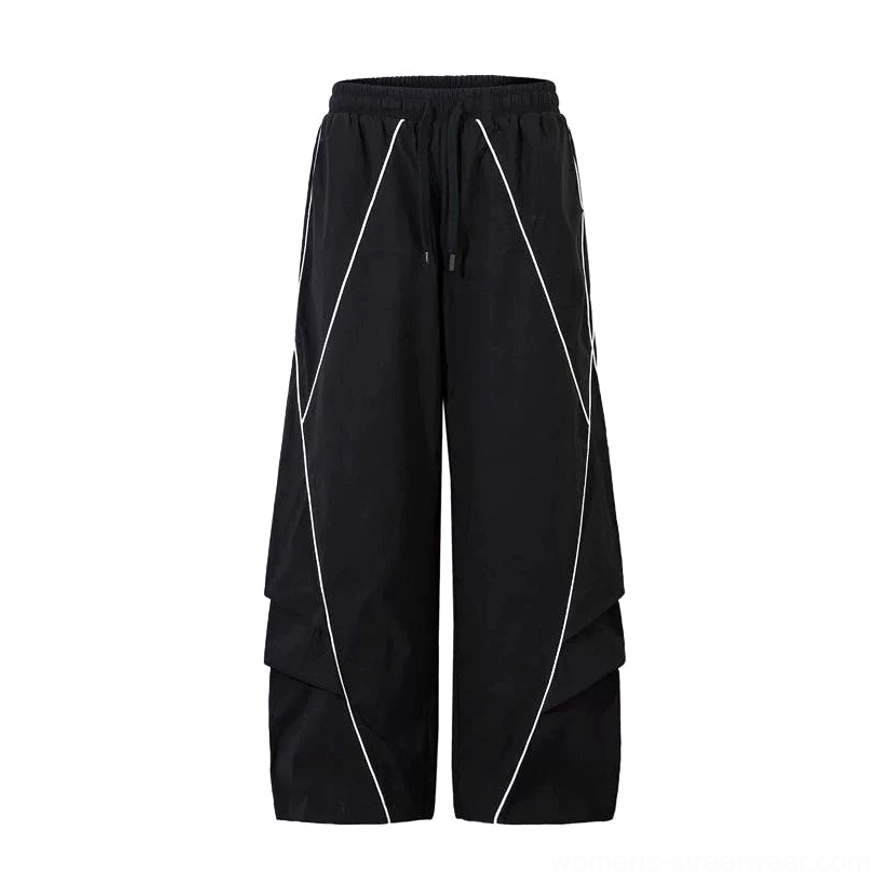 Flat lay of black reflective wide-leg cargo pants with elastic drawstring waist, visible white reflective piping, utility pocket detail, and relaxed streetwear construction