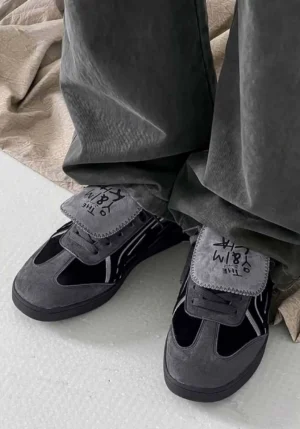 Black retro trainer sneakers worn with loose grey cargo pants, showing the low-profile streetwear silhouette and detachable graphic tongue panels