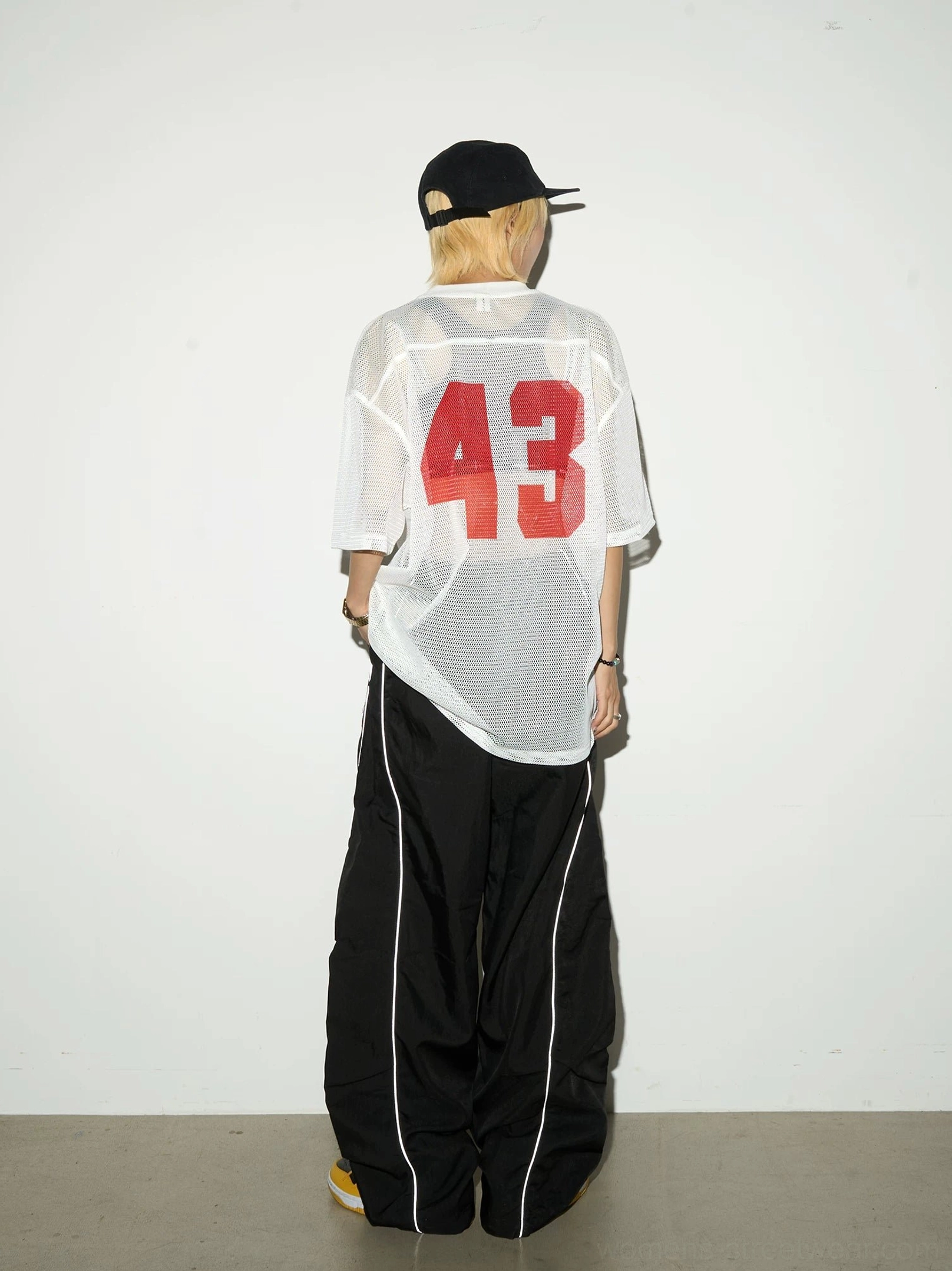 Back view of black reflective utility cargo pants with wide-leg streetwear fit and silver side detailing styled with an oversized sports tee in a minimalist studio