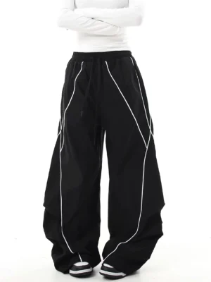 Black reflective streetwear cargo pants shown from the front with ultra-baggy wide-leg fit, elastic drawstring waist, curved seams, and contrasting reflective trim