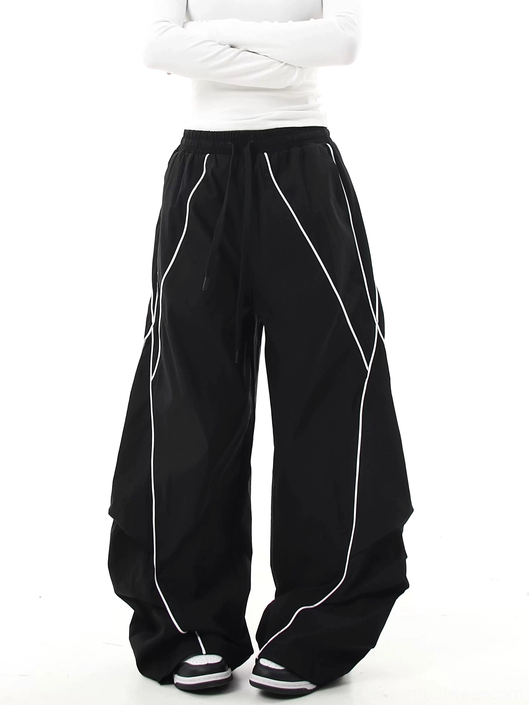 Black reflective streetwear cargo pants shown from the front with ultra-baggy wide-leg fit, elastic drawstring waist, curved seams, and contrasting reflective trim