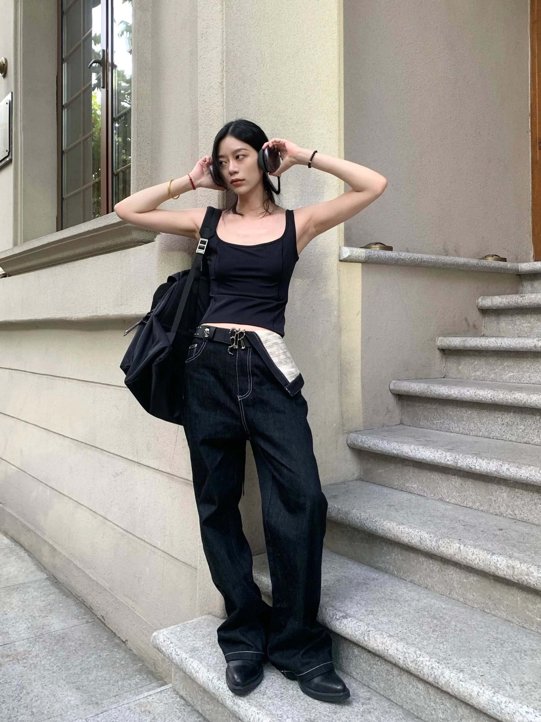Side view of black relaxed straight-leg denim jeans with asymmetric contrast waistband styled with a shoulder bag