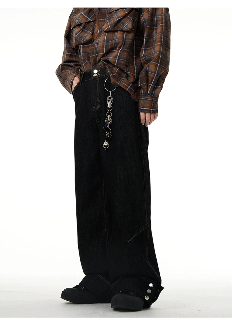 Three-quarter rear view of relaxed black wide-leg denim jeans with buttoned hems and decorative chain accessory