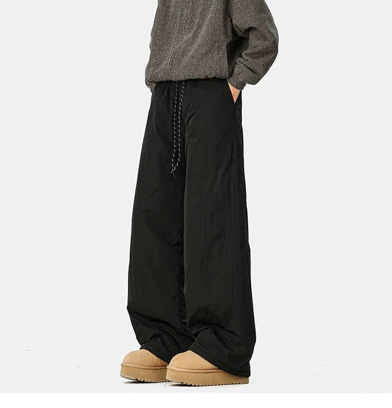 Side view of black relaxed wide-leg streetwear pants with crinkled polyester fabric, drawstring waist, pockets, and winter boots