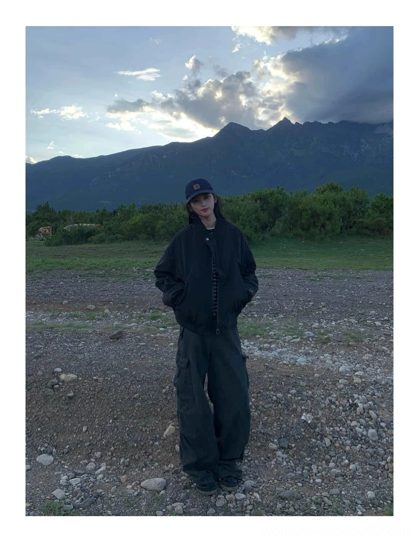 Relaxed black zip-up flight bomber jacket shown in a three-quarter view at dusk with mountain scenery