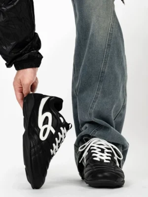 Black retro low-top streetwear sneakers shown from a front-side angle with smooth coated leather upper, white graphic side detail, white laces, and washed blue jeans styling