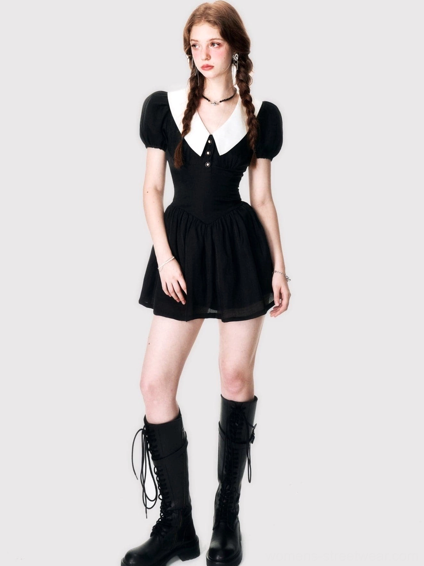 Full front view of a black retro mini dress with white pointed collar, short puff sleeves, fitted waist, flared skirt, and knee-high lace-up boots