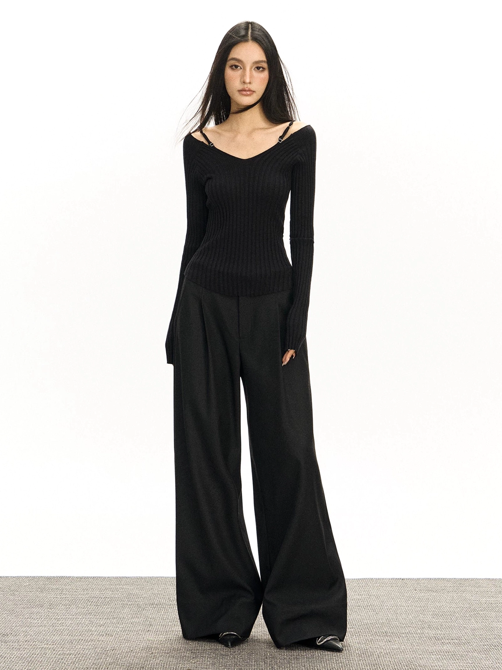 Full-body front view of black retro wide-leg tailored streetwear trousers styled with an off-shoulder fitted knit top and pointed-toe shoes