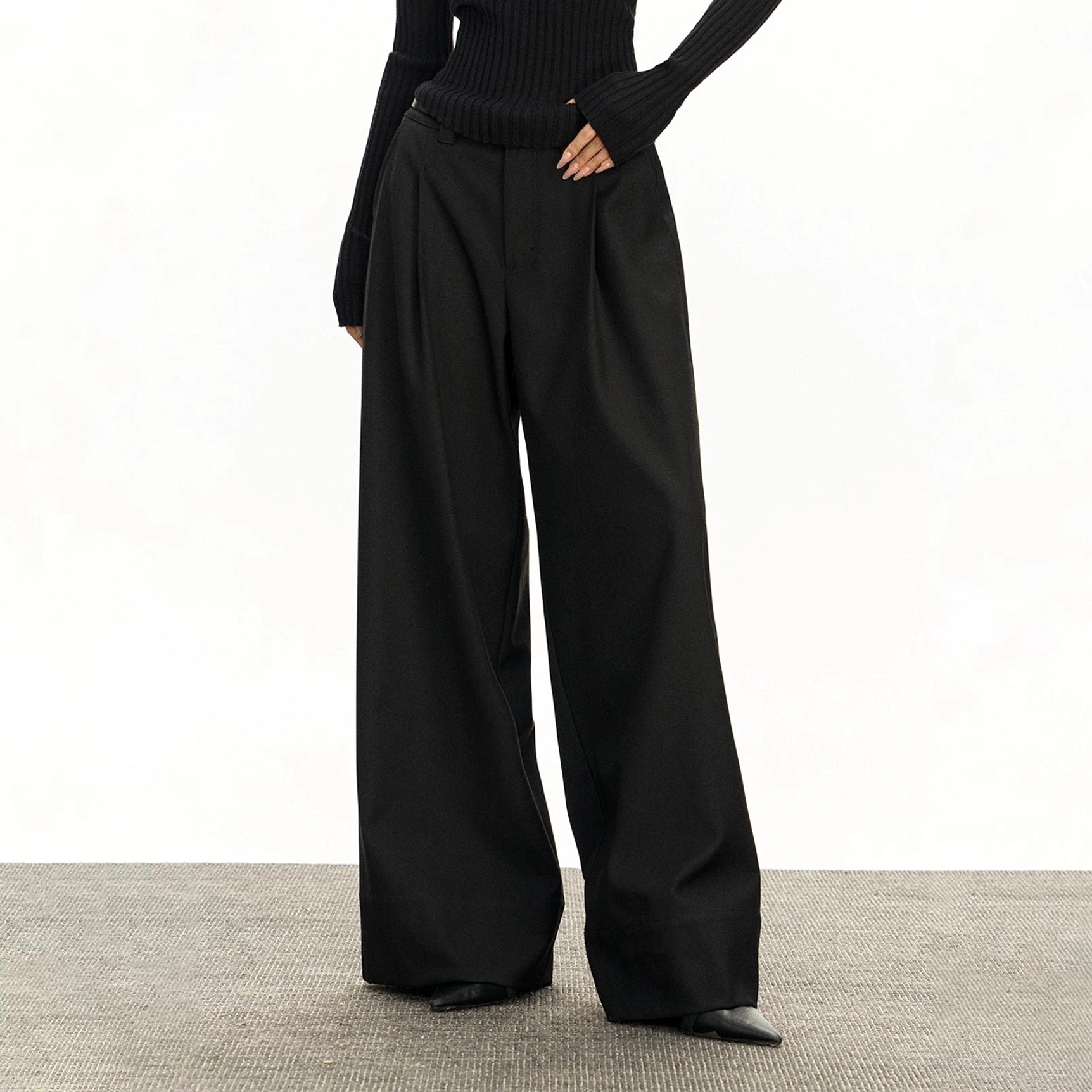 Black retro wide-leg tailored streetwear trousers styled with a slim black knit top, featuring a high-rise waist, front pleats, and structured suiting fabric