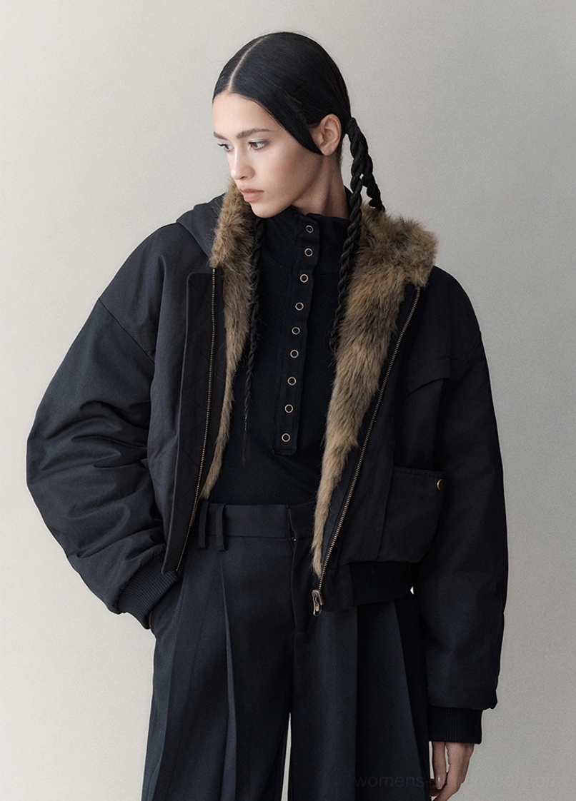 Side front view of a black hooded reversible winter jacket showing its relaxed sleeves, oversized fit, and faux fur collar trim