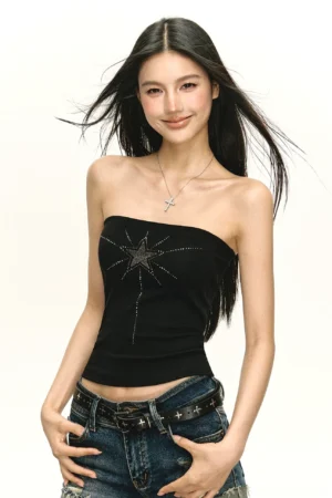 Three quarter front view of a black rhinestone starburst strapless corset top styled with low rise denim jeans and a cross pendant necklace in Y2K streetwear fashion