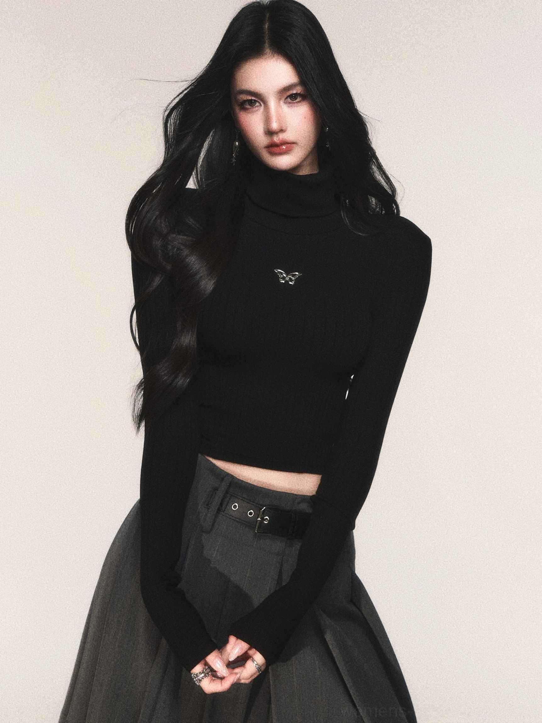 Black ribbed cropped turtleneck knit top with butterfly emblem styled with grey pleated midi skirt and belt