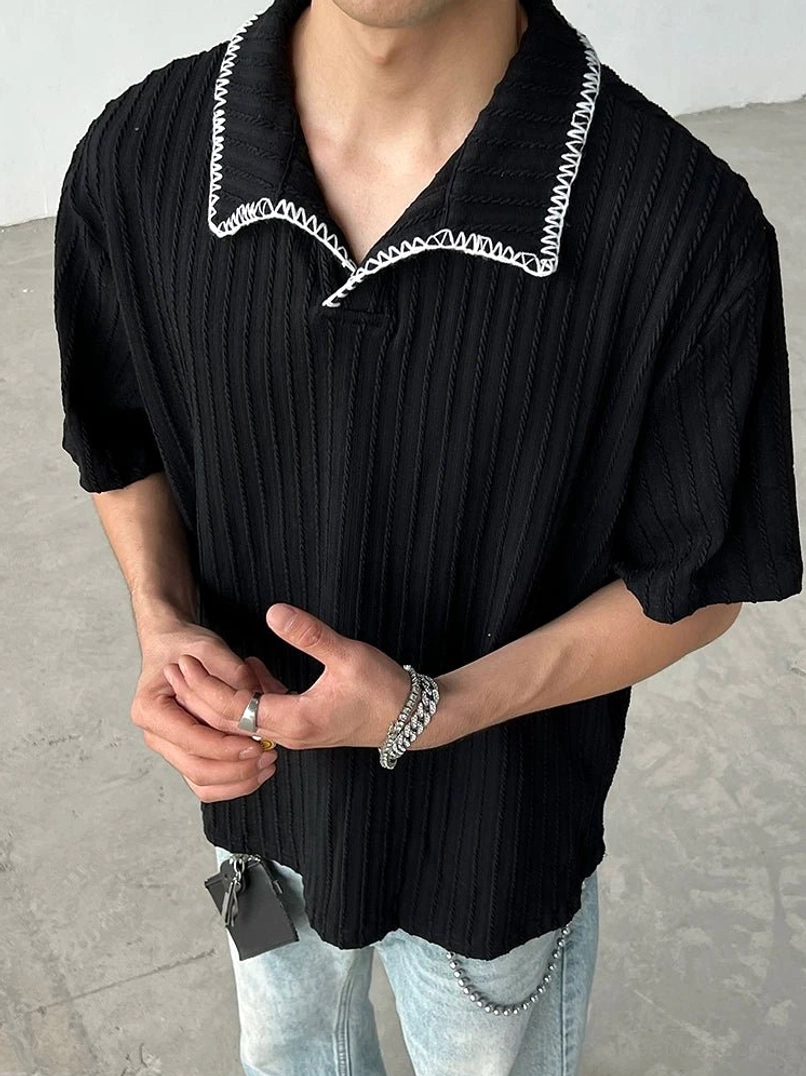 Black ribbed knit polo shirt close-up with white contrast blanket stitch collar and relaxed streetwear styling