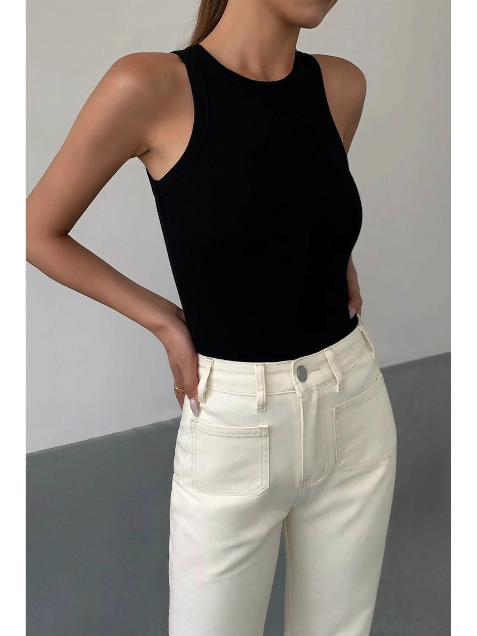 Black ribbed knit tank top front half-body shot on female model, paired with off-white straight leg jeans, sleeveless crew neck design focus